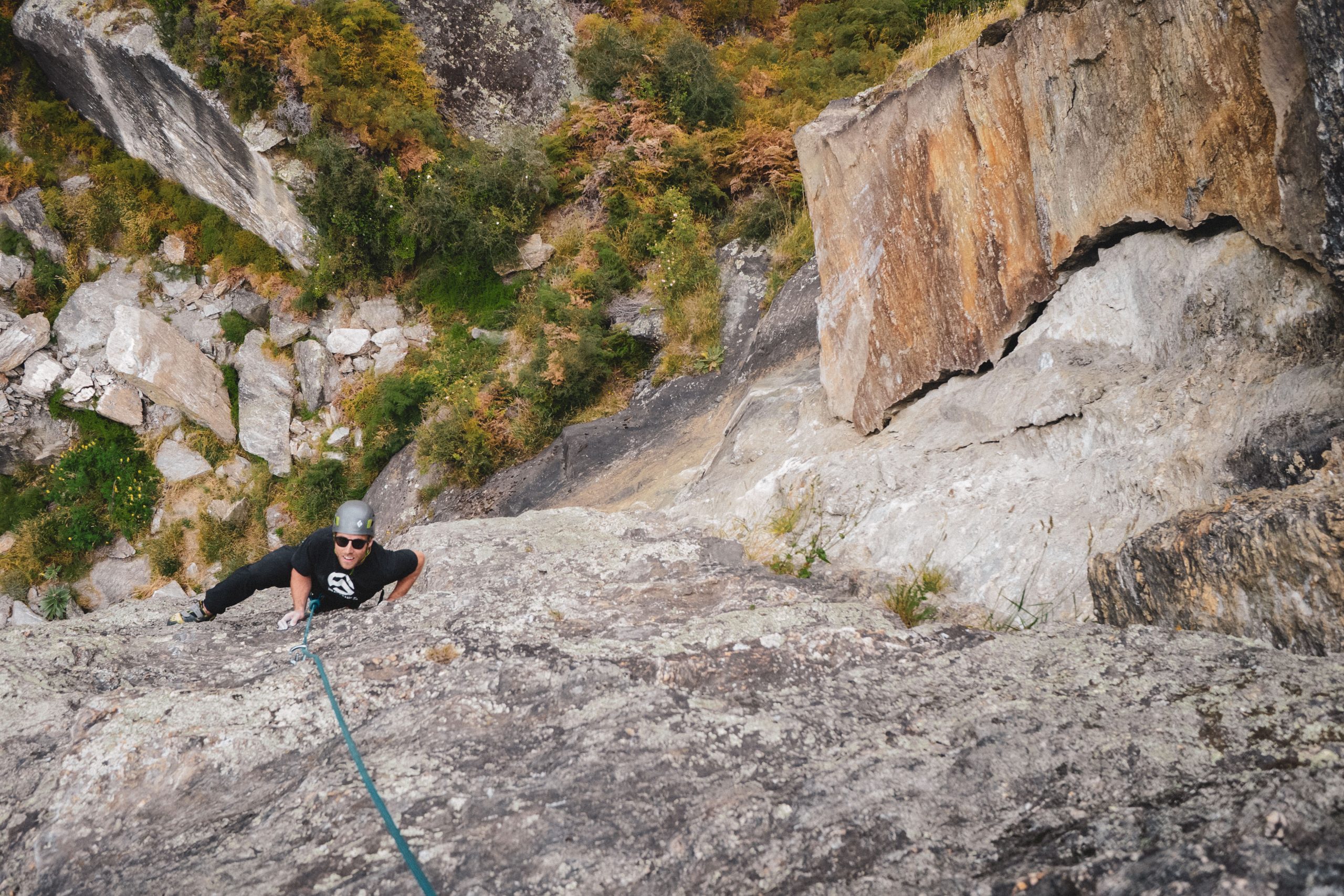 Rock climber scaling a vertical cliff face with ropes and helmet in a rugged outdoor setting near Wānaka.