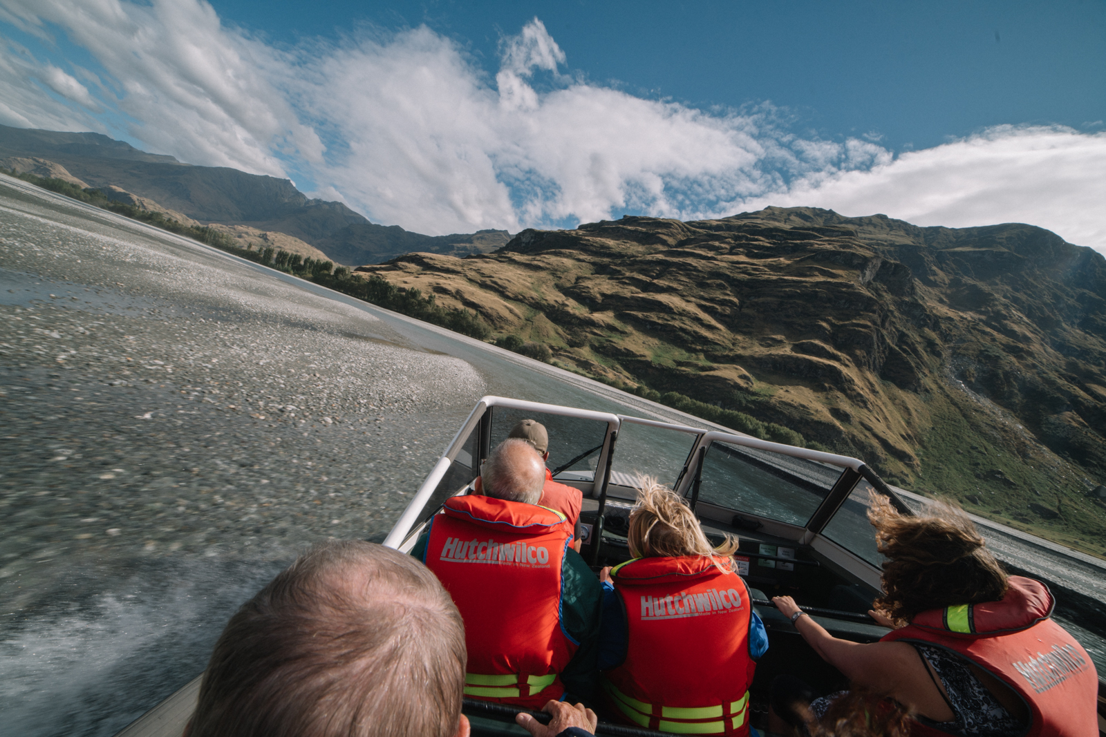 People in life jackets enjoying a high-speed jet boat ride through a braided river in Makarora New Zealand.
